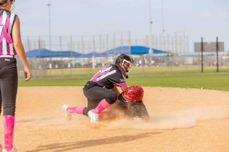 A softball player slides onto base while another player tries to fall on her and tag her out.