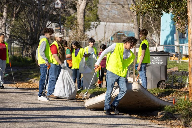 Teens carrying bulky trash and bags of litter on a neighborhood street