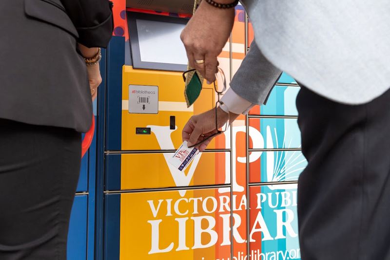 A person scans a library card at a vibrant locker with multiple doors