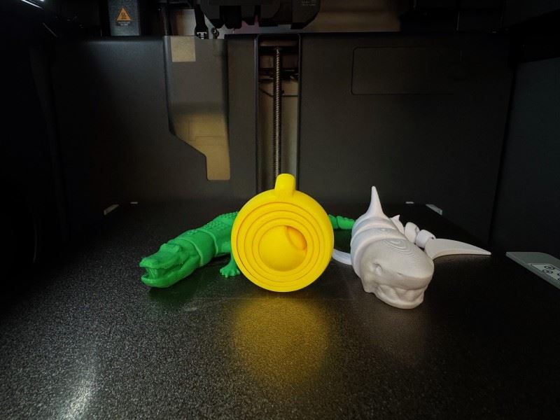 Three items created from a 3D printer including an articulated alligator and shark, and a puzzle. 