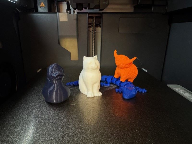 Four items created from a 3D printer including a cat, ox, duck, and articulated alligator.