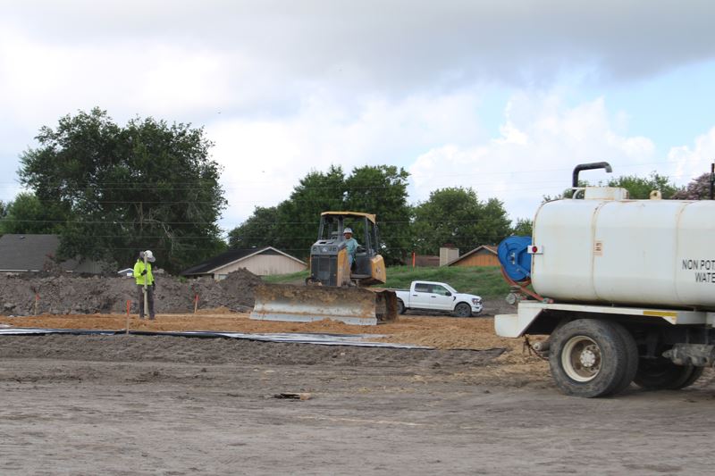 Construction workers driving heavy equipment at a leveled dirt work site