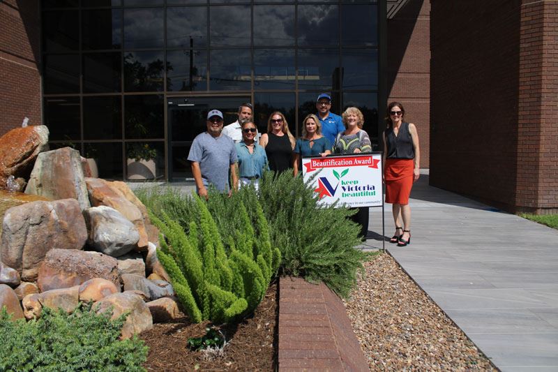 Group photo with KVB sign near a plant bed with a decorative stone fountain in the middle