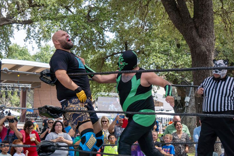 A luchador wearing a black and green outfit hits another fighter in the chest