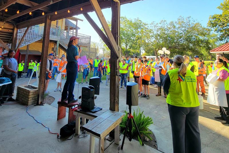 Christy Youker holding a microphone to address a crowd at the Victoria Art League building