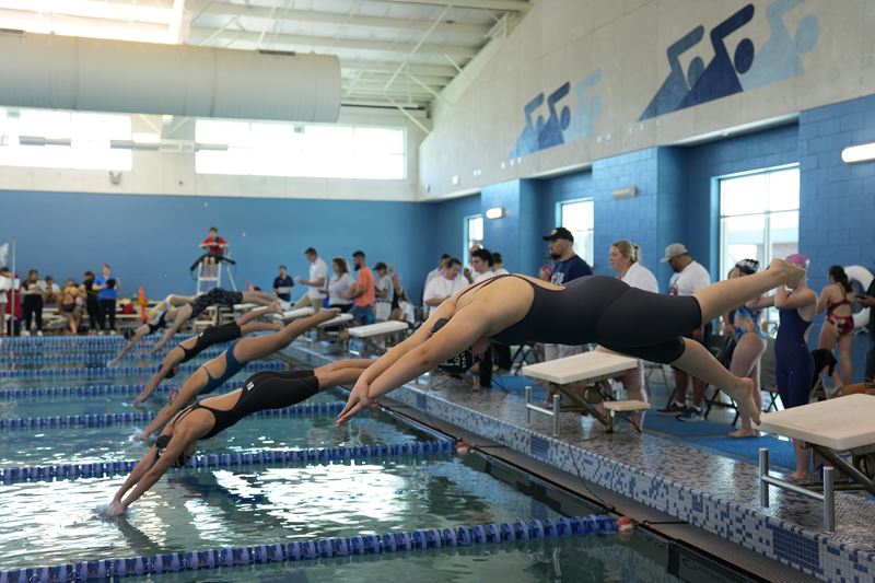 A row of swimmers dive into the pool at the Victoria ISD Aquatics Center