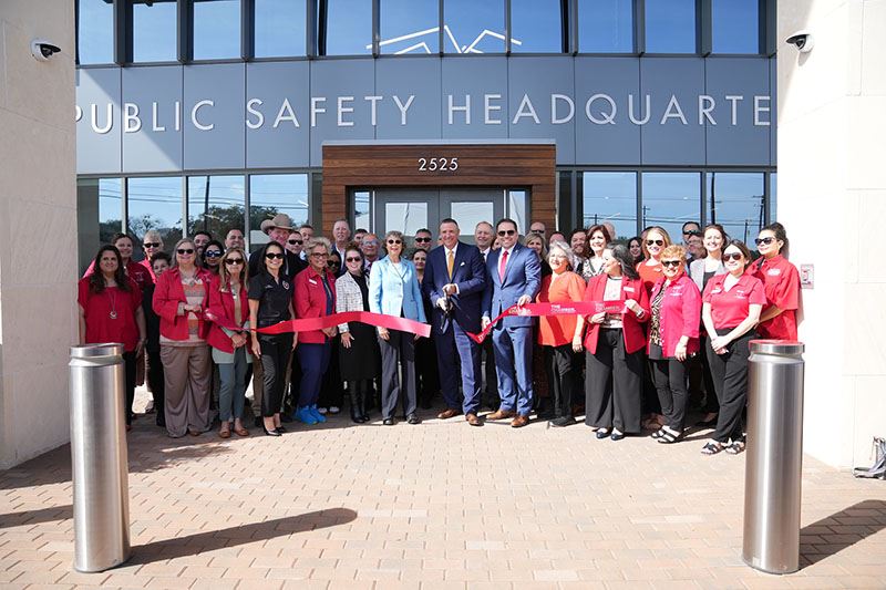 Large group of people cut a ceremonial red ribbon in front of the Public Safety Headquarters