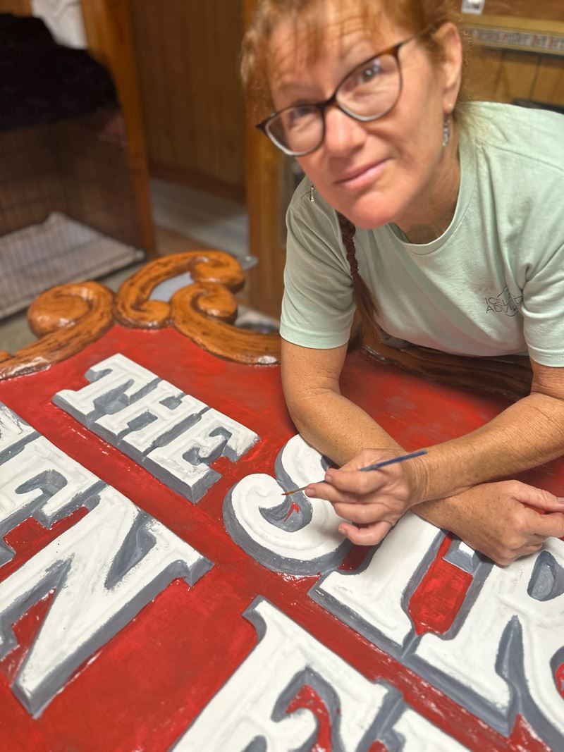 Debra Chronister uses a small brush to apply red paint to the crook of a letter S on a sign
