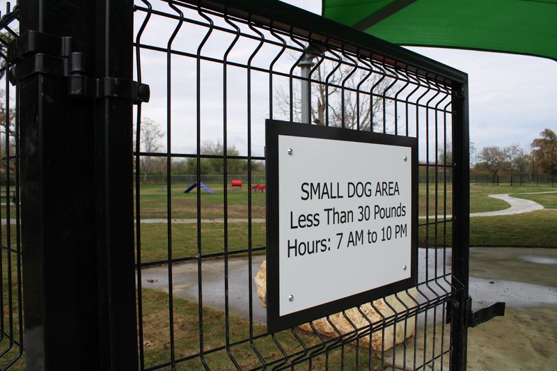 A sign on a gate says Small dog area. Less than 30 pounds. Hours. 7 a.m. to 10 p.m.