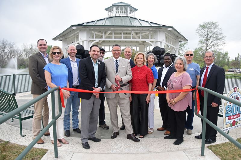 Large group photo of people cutting a red ribbon in front of the Riverside Park duck pond gazebo