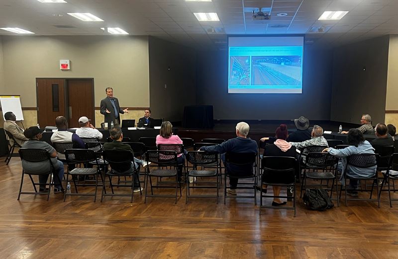 About a dozen people sit in folding chairs and watch a PowerPoint at the Community Center annex
