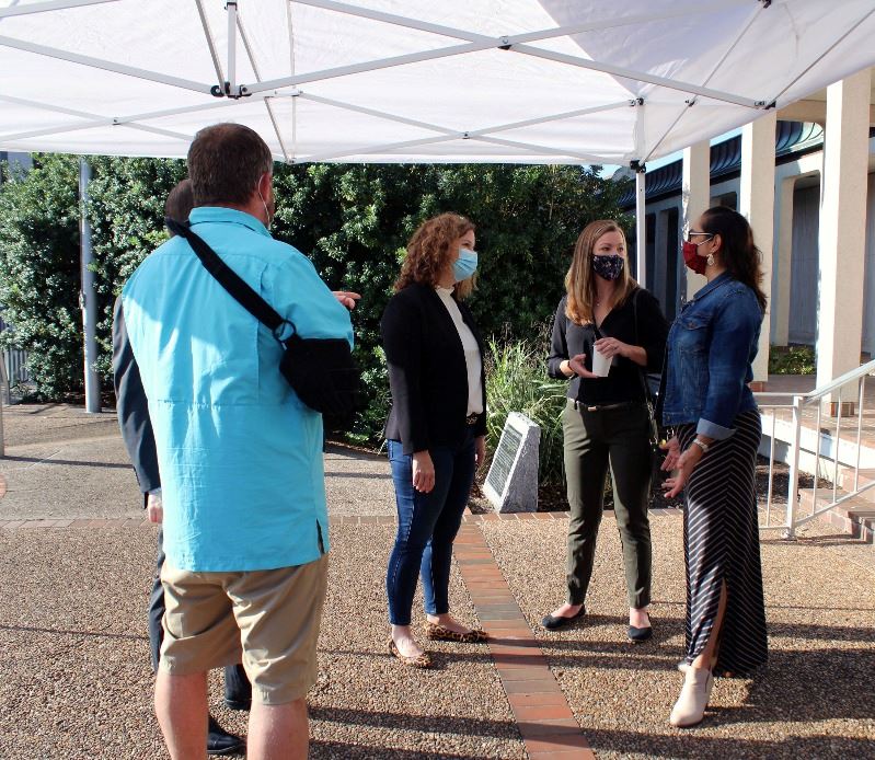 People in masks visit beneath a canopy in front of the Municipal Court building.